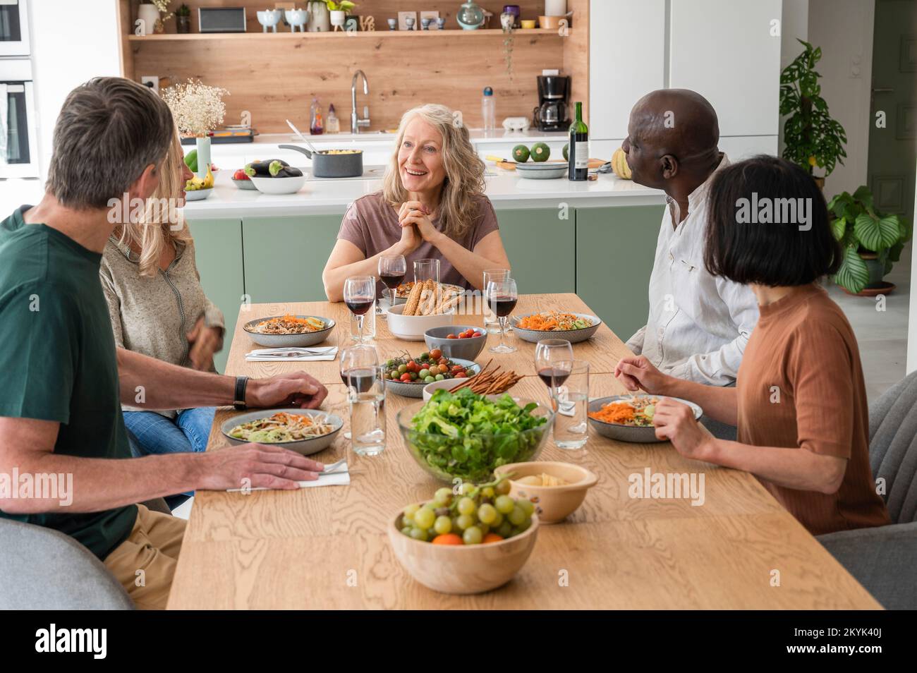 Eine Gruppe von Freunden mittleren Alters, die Geschichten erzählen, während sie zu Hause zu Mittag essen Stockfoto