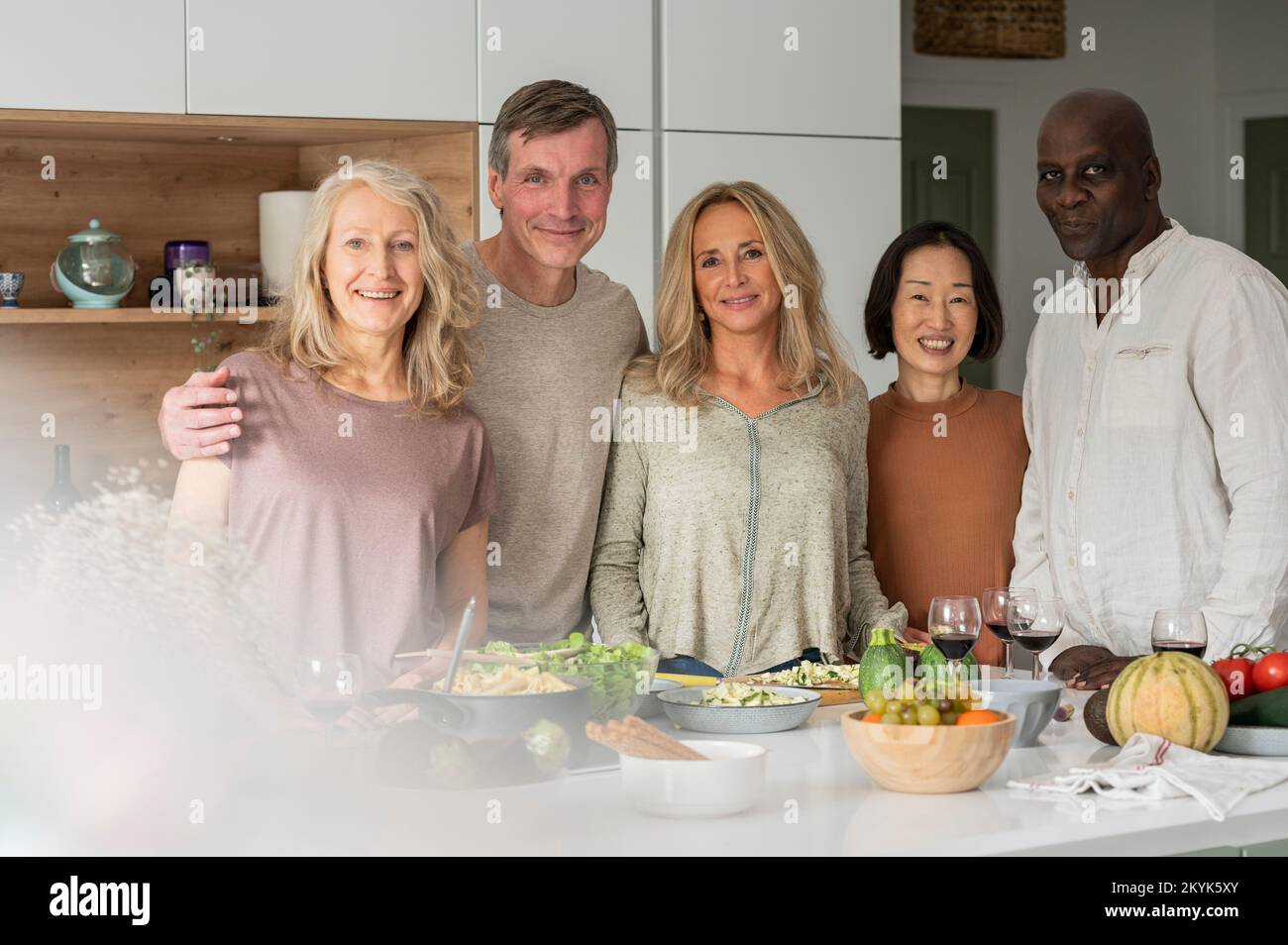Gruppenporträt verschiedener älterer Freunde, die nach dem Kochen auf der Kücheninsel stehen Stockfoto