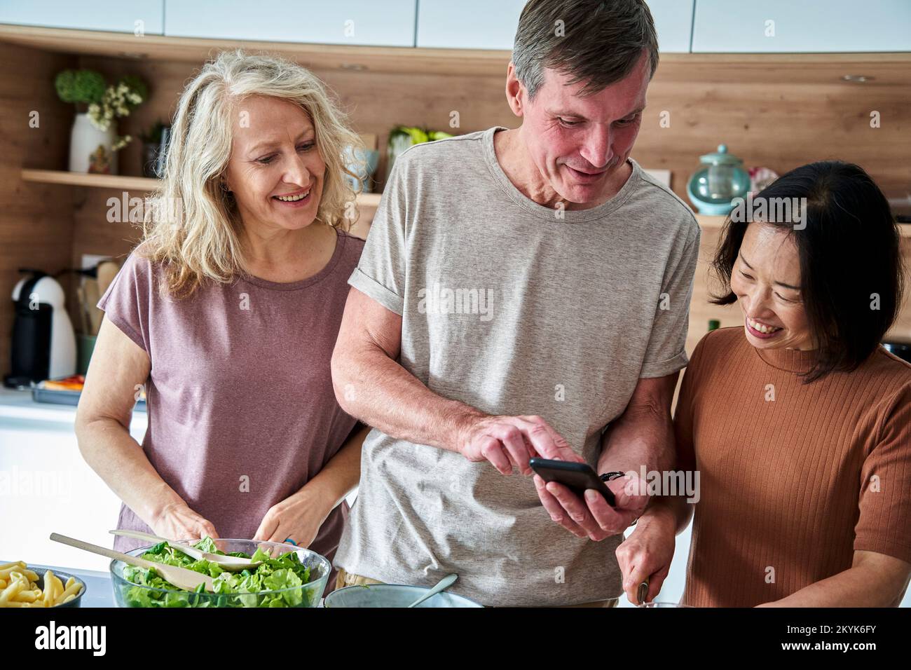 Älterer Mann, der ein Smartphone benutzt, während er mit Freunden in der Küche spricht Stockfoto
