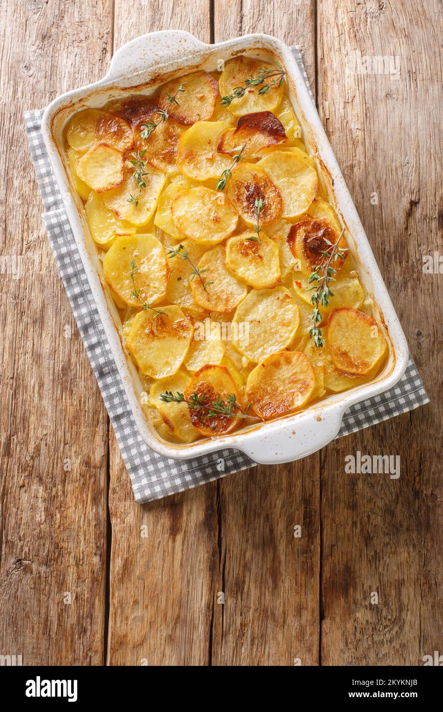 Schneidet Kartoffelauflauf mit Zwiebeln, frischem Thymian und Butter in der Backform auf dem Tisch. Vertikale Draufsicht von oben Stockfoto