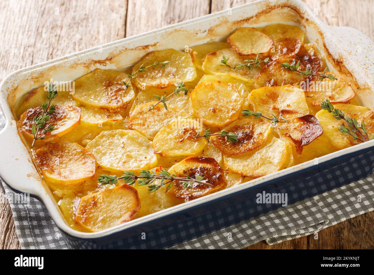 Französischer Kartoffelauflauf mit Gemüsebrühe, Kräutern, Zwiebeln und Knoblauch in Nahaufnahme in einem Backblech auf einem Holztisch. Horizontal Stockfoto