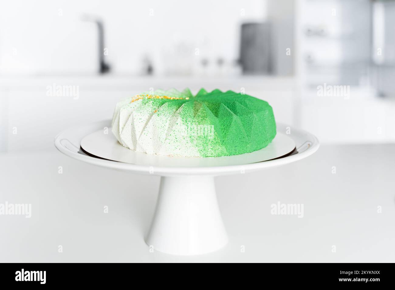 In der weißen Küche auf dem Tisch ist ein grüner Moussekuchen auf einem weißen Ständer mit einem Bein Stockfoto