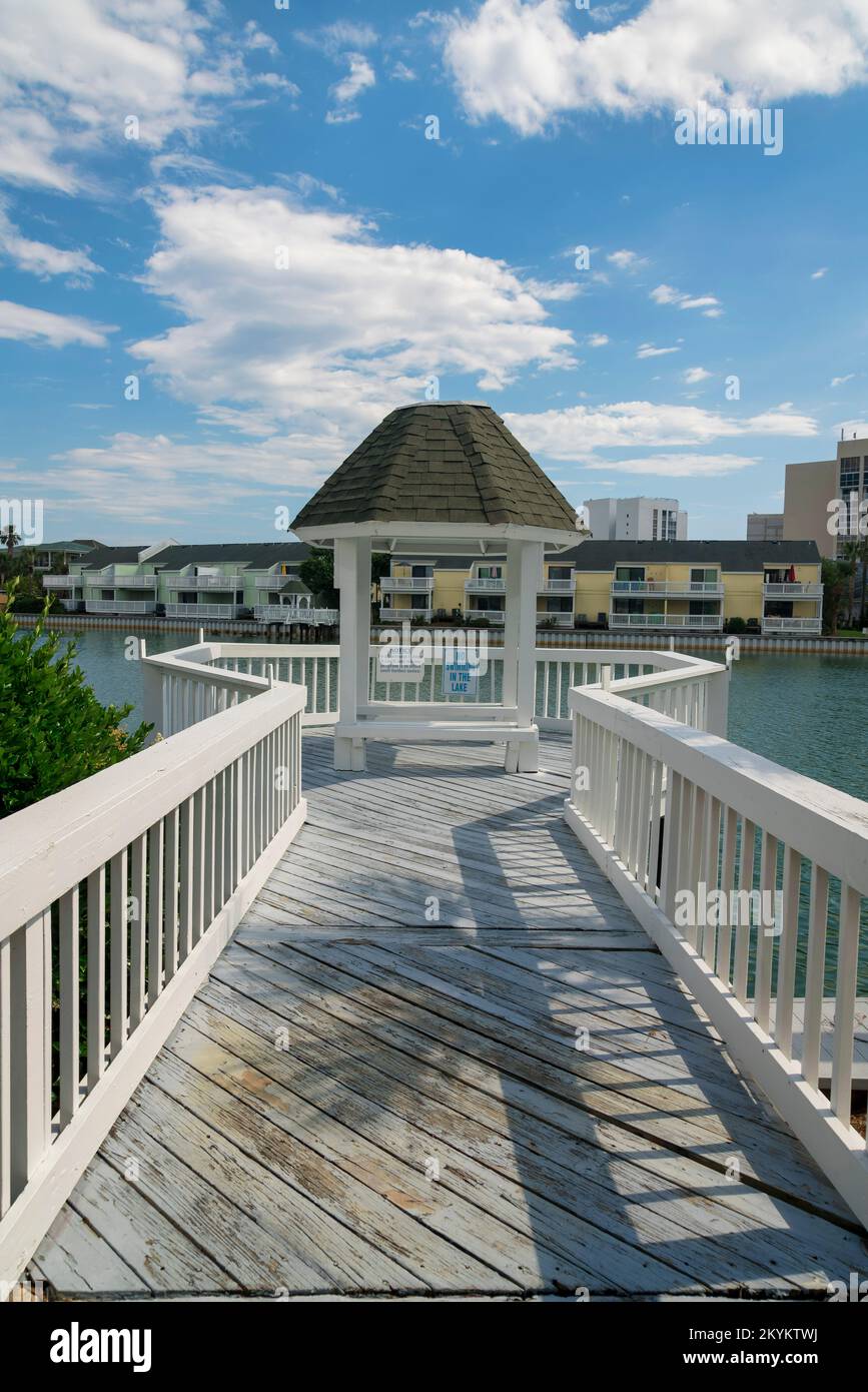 Pfad mit weißen Geländern führt zu einem kleinen Pavillon über dem See mit Brackwasser - Destin, FL. Es gibt einen Blick auf weiße Wolken im blauen Himmel o Stockfoto