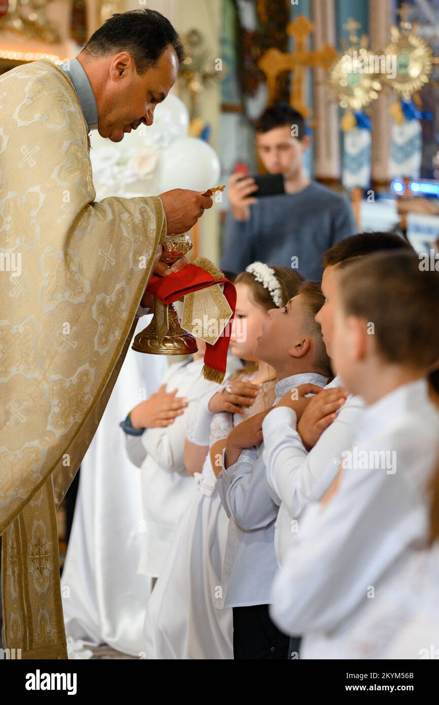 Ivano-Frankiwsk, Ukraine 21. Mai 2022: Erste Kommunion für Kinder, Priester gibt Kommunion für Kinder. Stockfoto