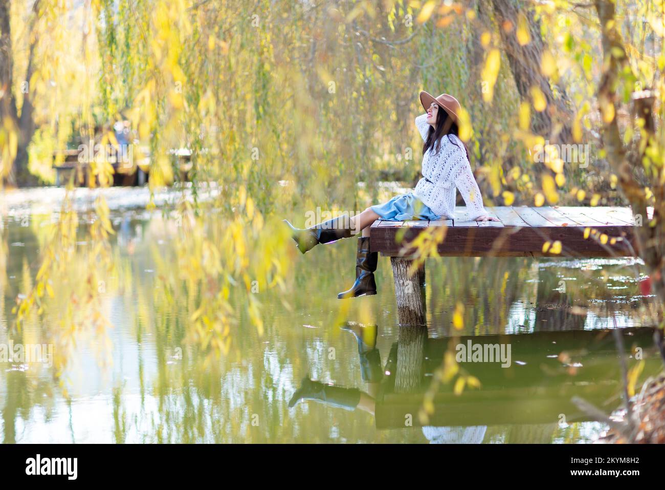 Herbstsee-Frau. Sie sitzt im Herbst an einem Teich auf einem hölzernen Pier und bewundert die Natur. Das Konzept des Tourismus, Wochenenden außerhalb der Stadt. Stockfoto