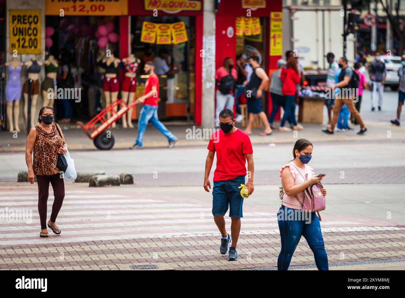 Fußgänger überqueren eine Straße, ein Mann trägt ein rotes Hemd, und Leute gehen auf dem Bürgersteig vor dem Laden in der Innenstadt von Belo Horizonte, Brasilien. Stockfoto