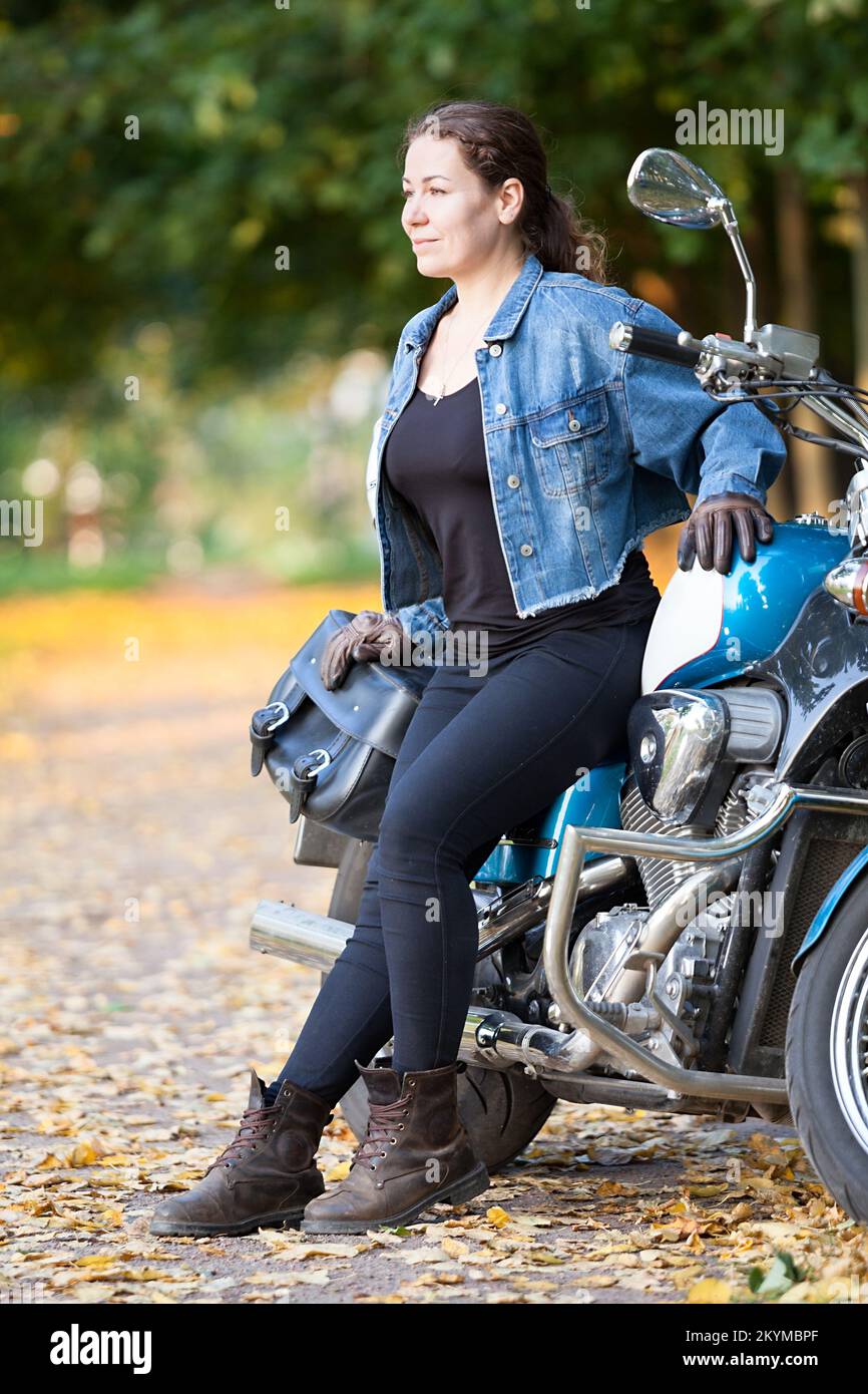 Ein Mädchen mit Jeansjacke und braunen Motorradhandschuhen sitzt auf einem klassischen Motorrad Stockfoto