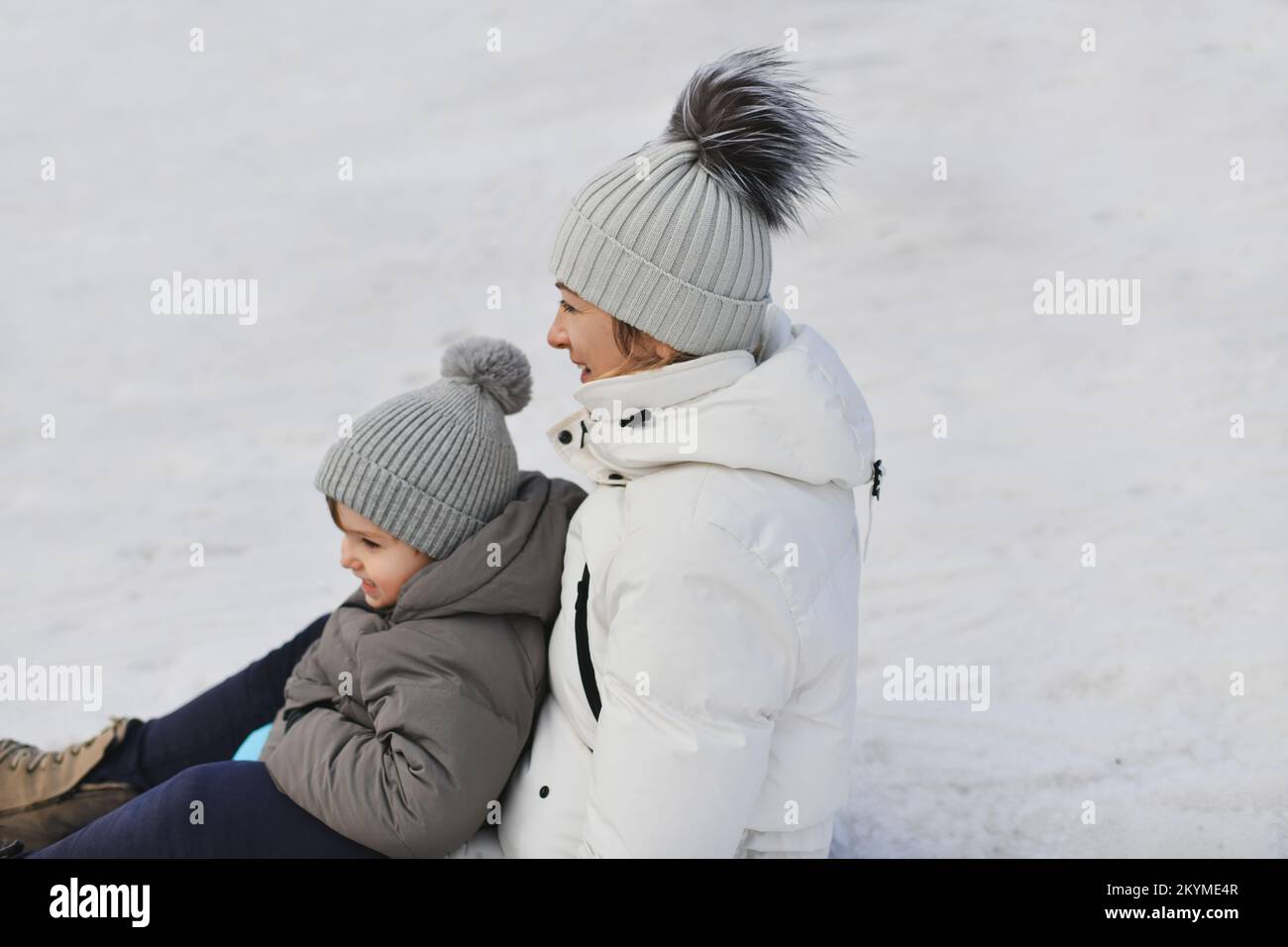 Eine Mutter mit Sohn, die im Schnee schlittenfährt Stockfoto