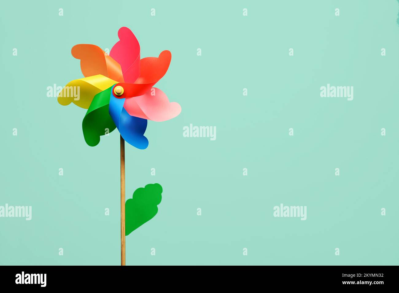 Mehrfarbiges, blumenförmiges Drehrad mit grünem Blatt auf hellem türkisfarbenem Hintergrund Stockfoto