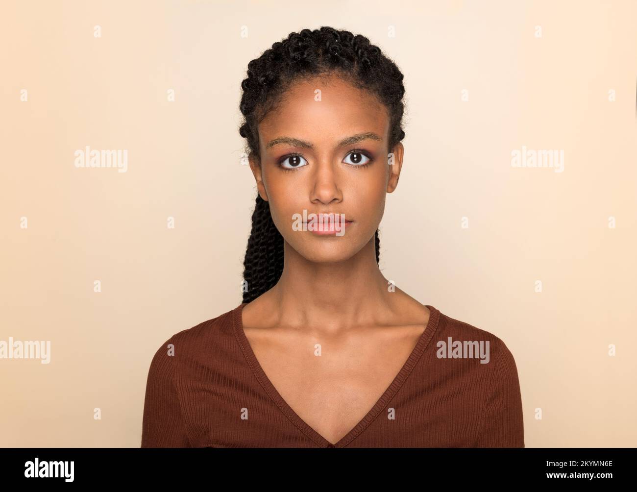 Porträt einer jungen afroamerikanischen Frau mit langen Afrogeflechten, die vor beigefarbenem Hintergrund in die Kamera schaut Stockfoto