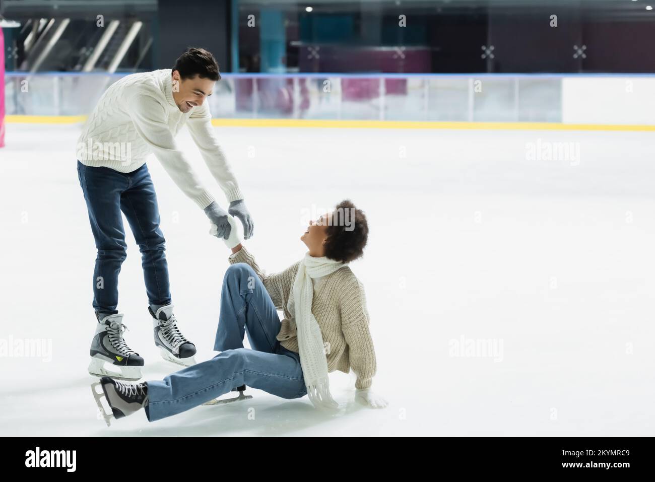 Ein lächelnder Mann, der einer afroamerikanischen Freundin auf der Eisbahn Hand reicht Stockfoto