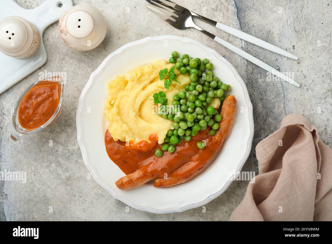 Knaller und Püree. Gegrillte Würstchen mit Kartoffelpüree und grüner Erbse auf weißem Teller auf grauem Hintergrund. Traditionelles Gericht aus Großbritannien und Irland. BB Stockfoto