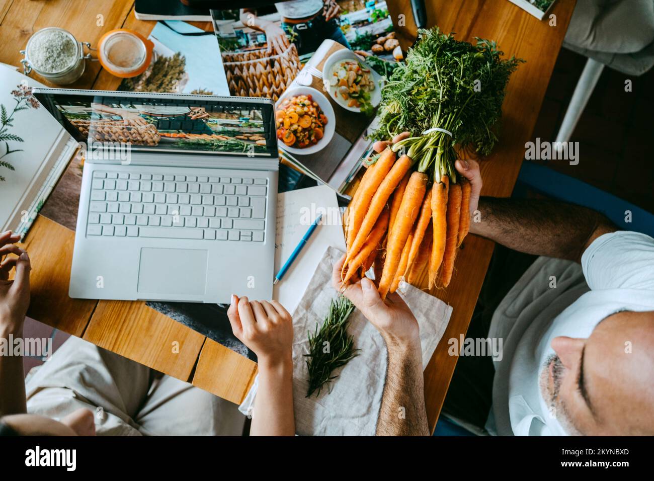 Männlicher Kollege hält einen Haufen Karotten von einem Unternehmer mit Laptop auf dem Tisch Stockfoto