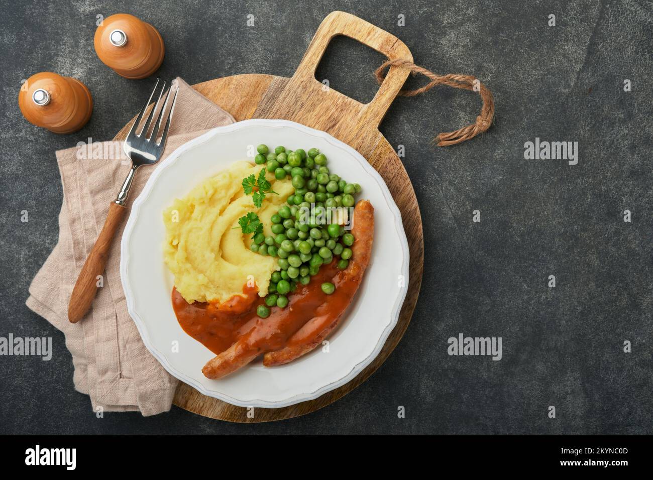 Knaller und Püree. Gegrillte Würstchen mit Kartoffelpüree und grüner Erbse auf weißem Teller auf schwarzem dunklem Hintergrund. Traditionelles Gericht aus Großbritannien und Irela Stockfoto