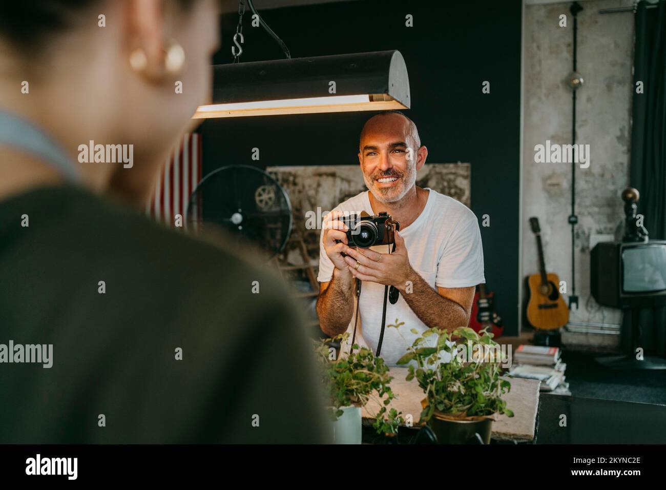Glücklicher männlicher Fotograf, der eine Digitalkamera hält, während er einen Kollegen im Studio ansieht Stockfoto