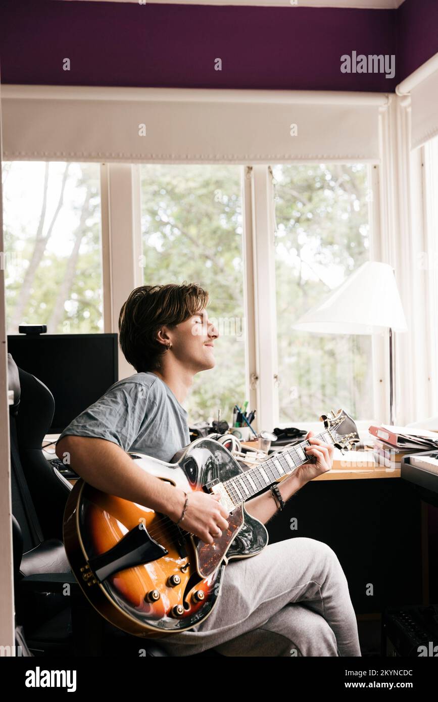Junger Mann mit geschlossenen Augen, der zu Hause Gitarre spielt Stockfoto