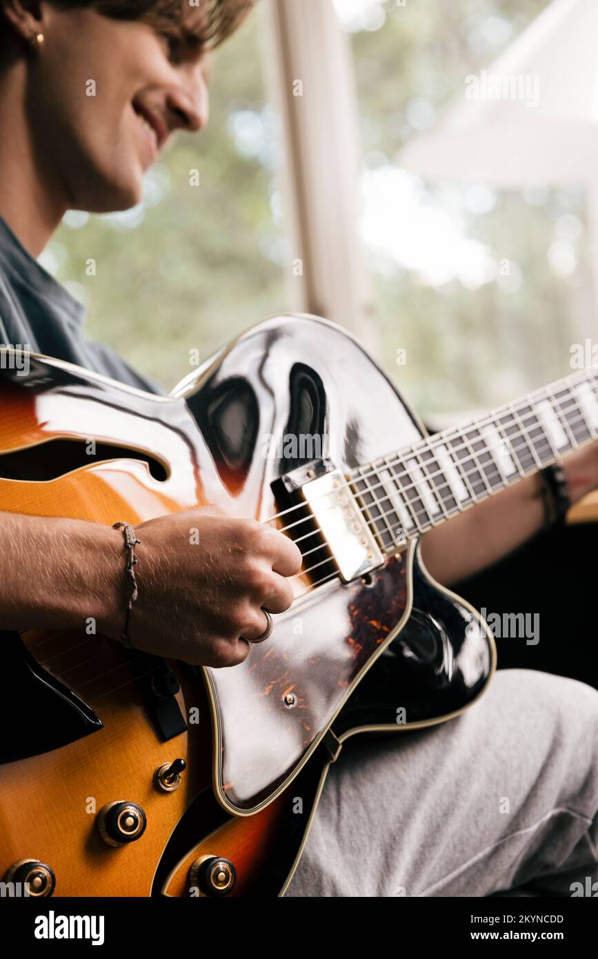 Die Hand eines lächelnden Mannes, der zu Hause Akkord auf der Gitarre spielt Stockfoto