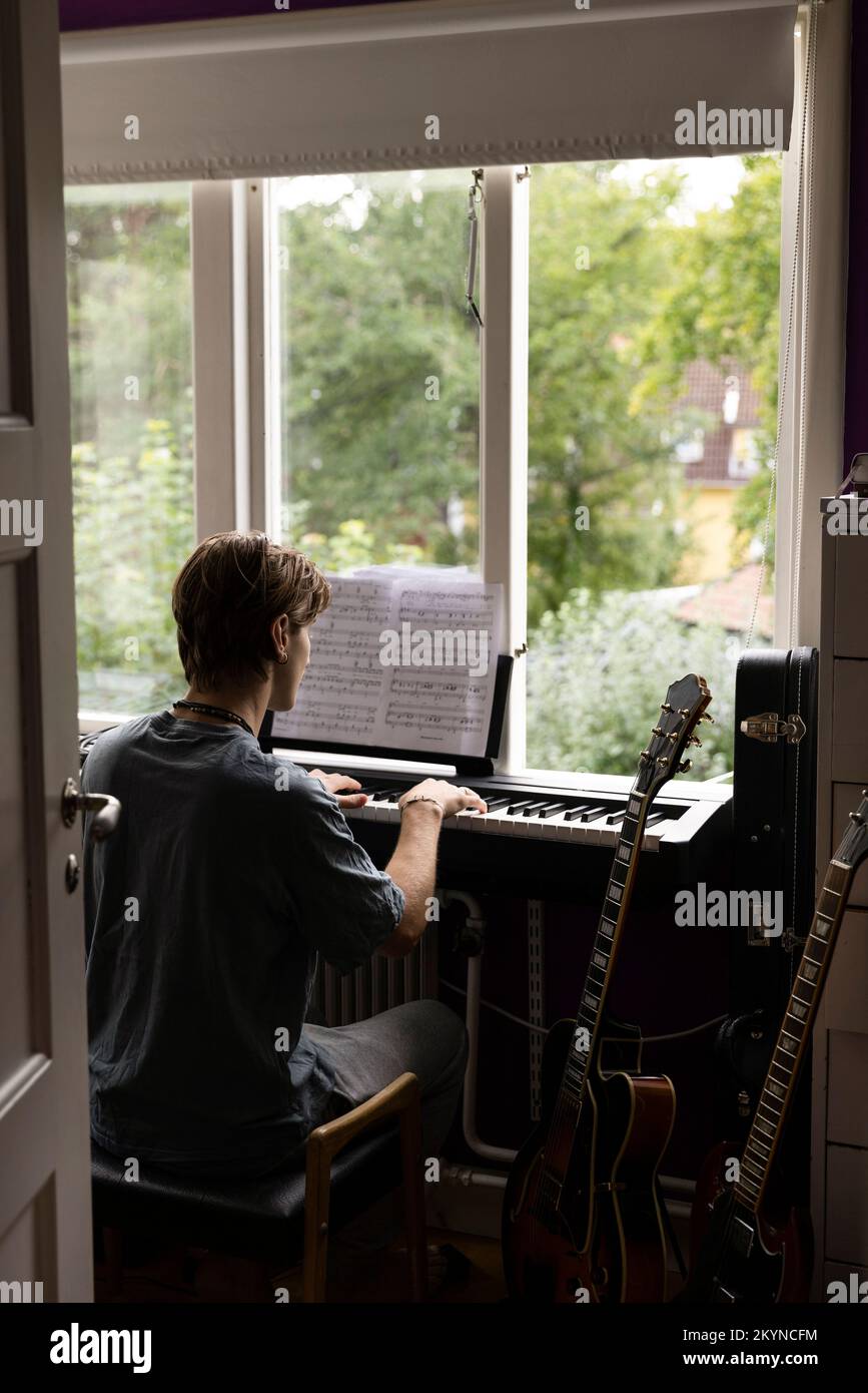 Rückansicht eines Mannes, der beim Klaviertraining zuhause eine Note liest Stockfoto