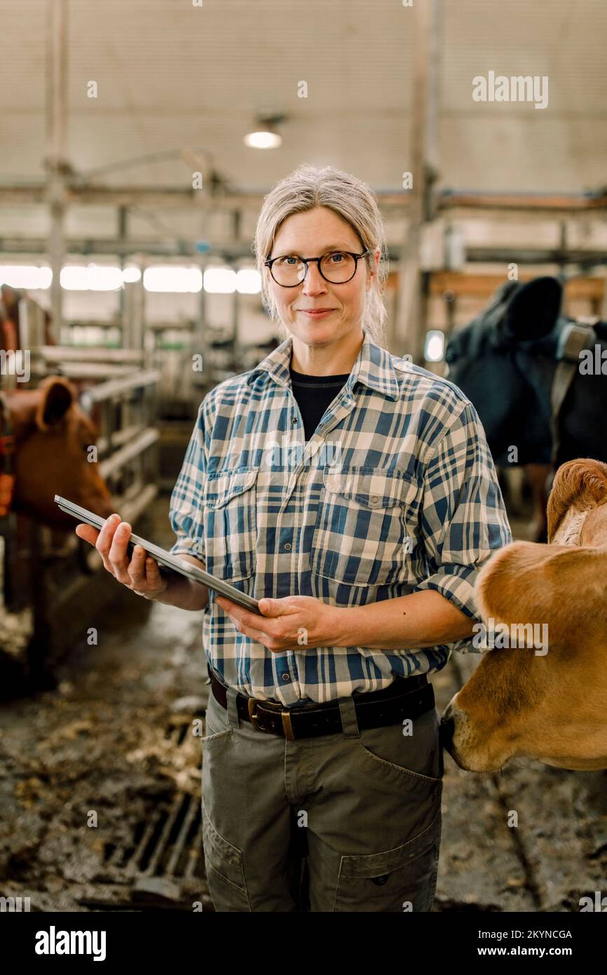 Lächelnde Landwirtin im Stehen mit Tablet-PC auf einer Rinderfarm Stockfoto