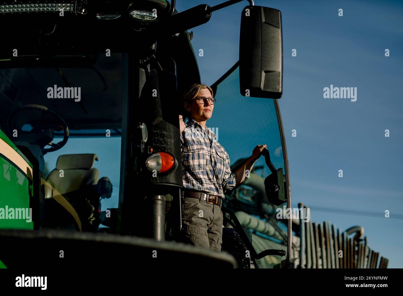Nachdenklicher Landwirt, der auf dem Traktor auf dem Hof steht Stockfoto