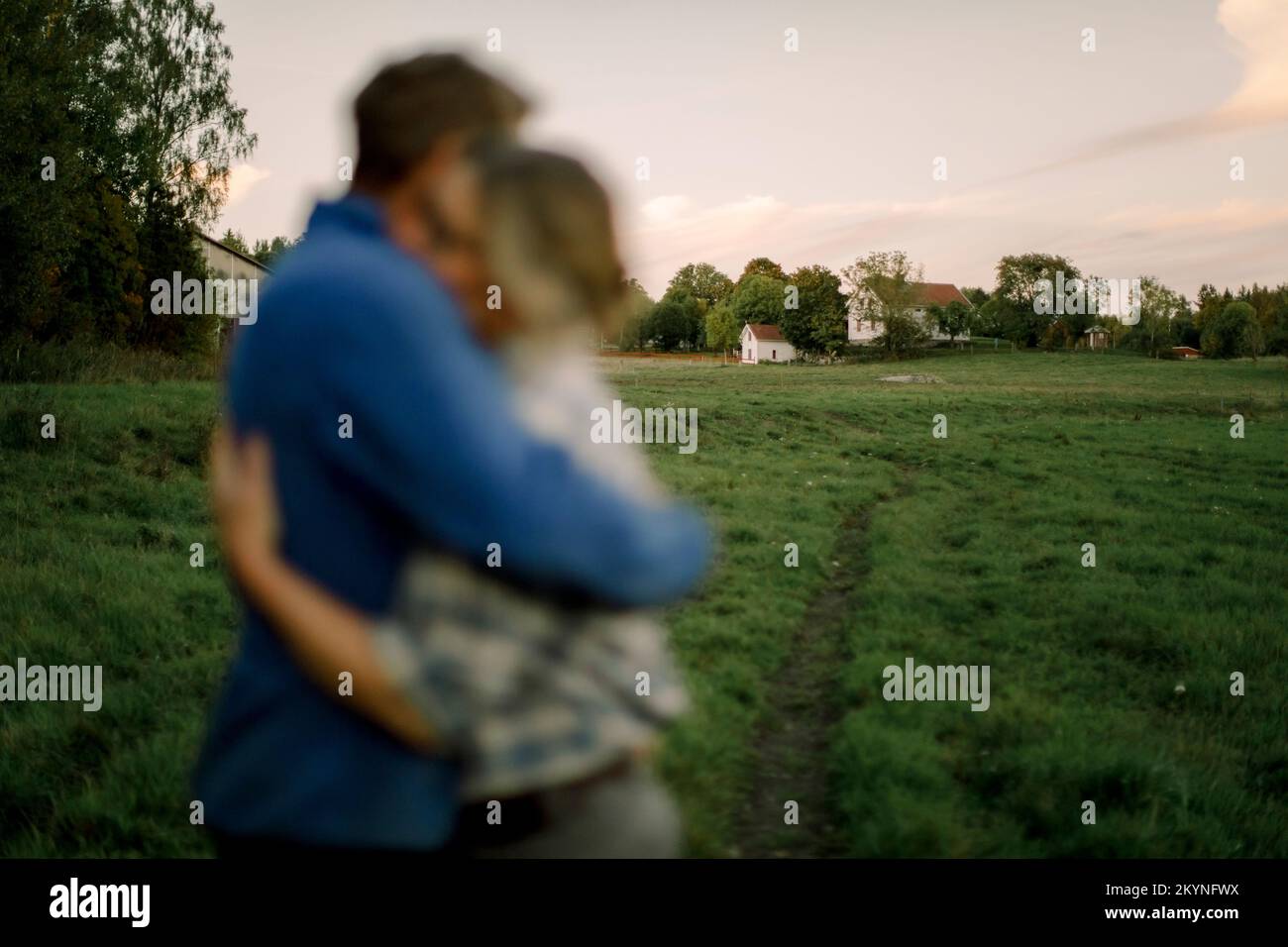 Ein Paar umarmt sich während des Sonnenuntergangs mit landwirtschaftlichen Feldern im Hintergrund Stockfoto