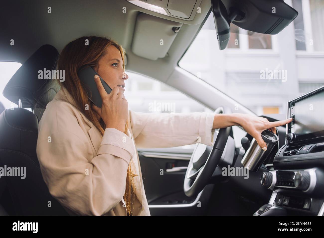 Unternehmerin, die über ein Mobiltelefon spricht, während sie im Auto eine Touchscreen-Bedienkonsole auf dem Armaturenbrett verwendet Stockfoto