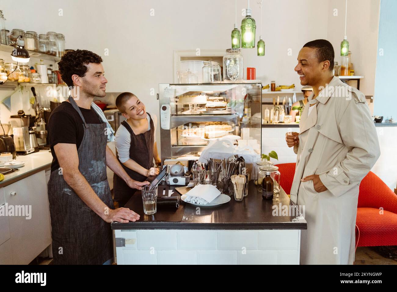 Lächelnder Gast, der mit männlichen und weiblichen Cafetetbesitzern an der Kasse interagiert Stockfoto