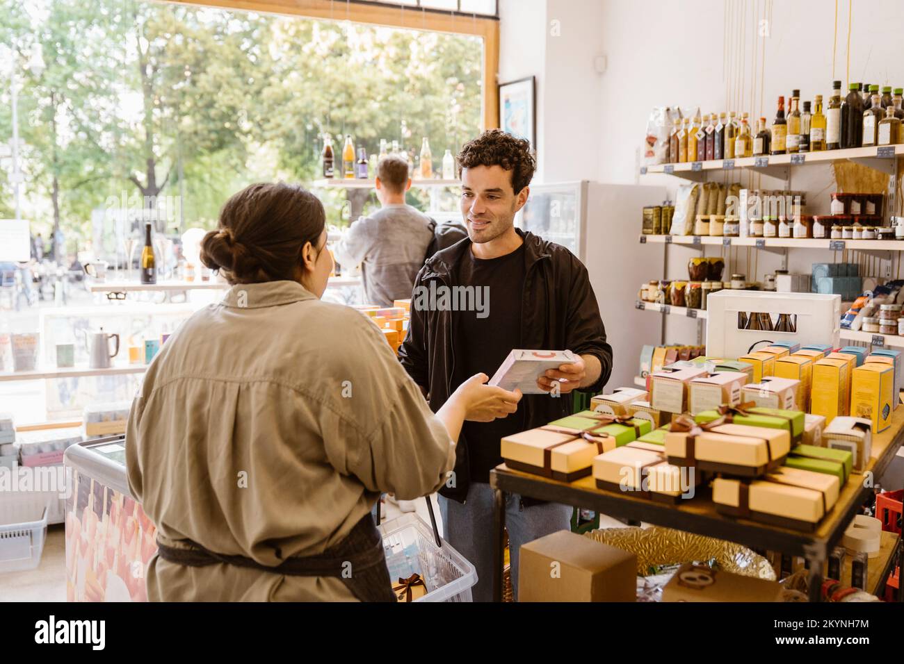 Männlicher Kunde kauft Lebensmittel, während er mit der Besitzerin im Geschäft spricht Stockfoto