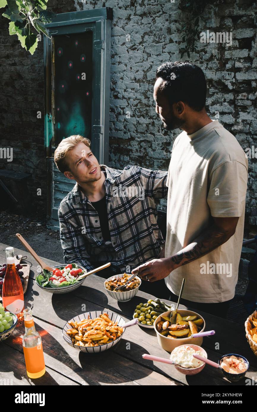 Junge männliche Freunde, die sich auf einer Gartenparty im Garten unterhalten Stockfoto