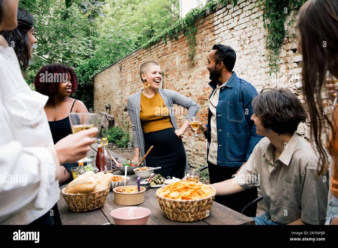 Junge Frau, die sich mit Freunden unterhalten hat, während sie sich im Garten versammelt hat Stockfoto