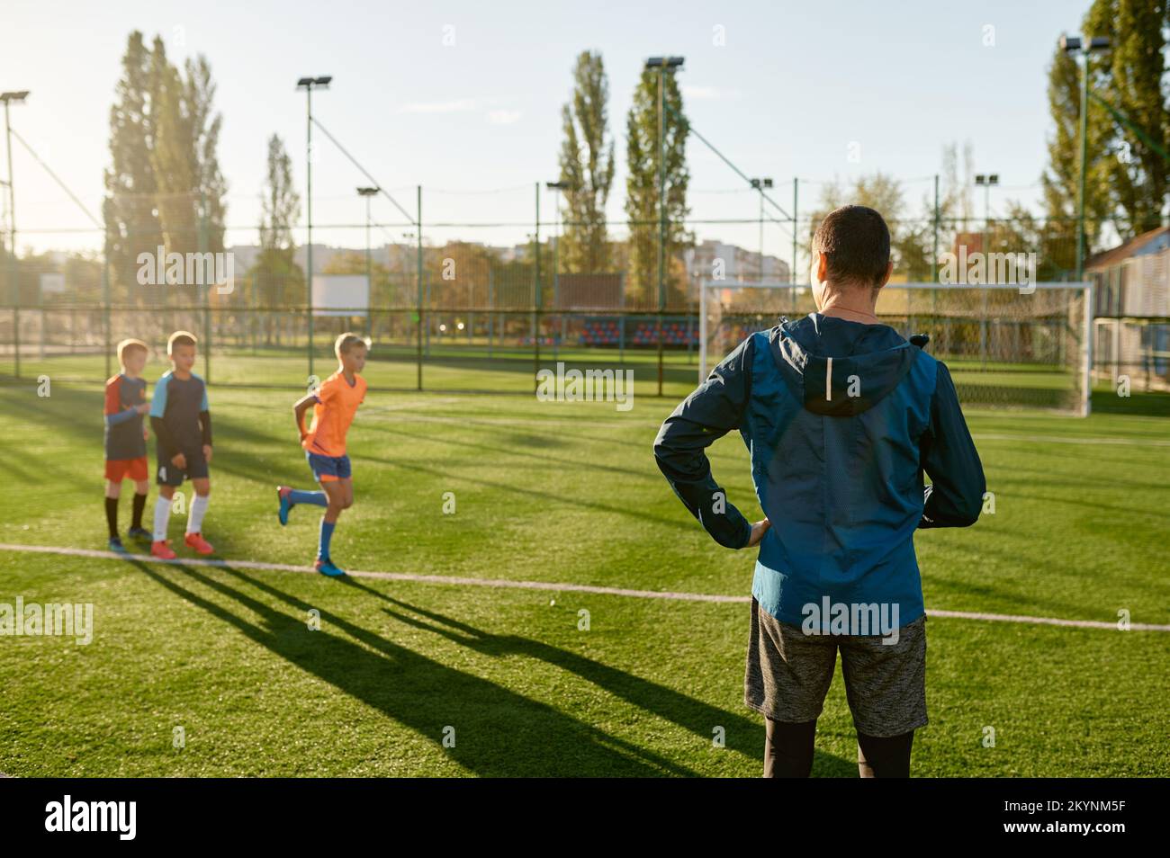 Kinder, die Fußball auf dem Rasenplatz unter der Kontrolle eines Fußballtrainers üben Stockfoto