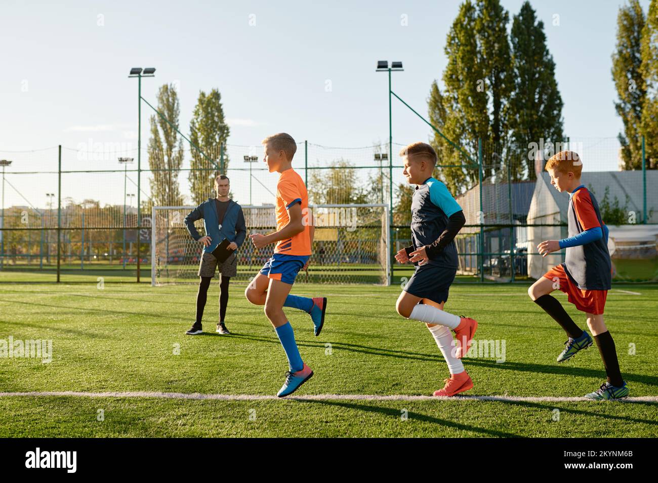 Kinder, die Fußball auf dem Rasenplatz unter der Kontrolle eines Fußballtrainers üben Stockfoto