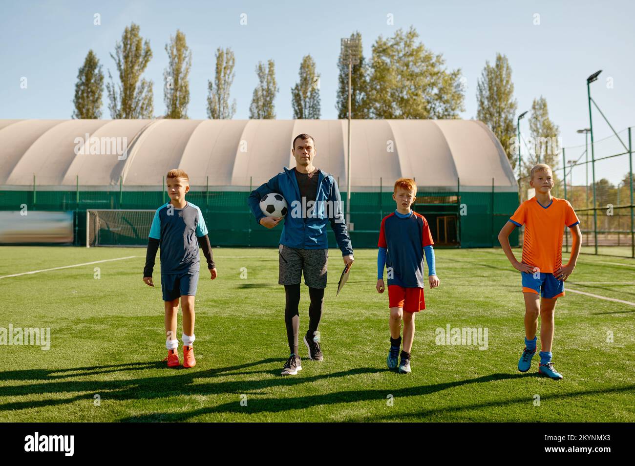 Hübsche Trainerin und Junior-Fußballmannschaft, die über das Spielfeld laufen Stockfoto