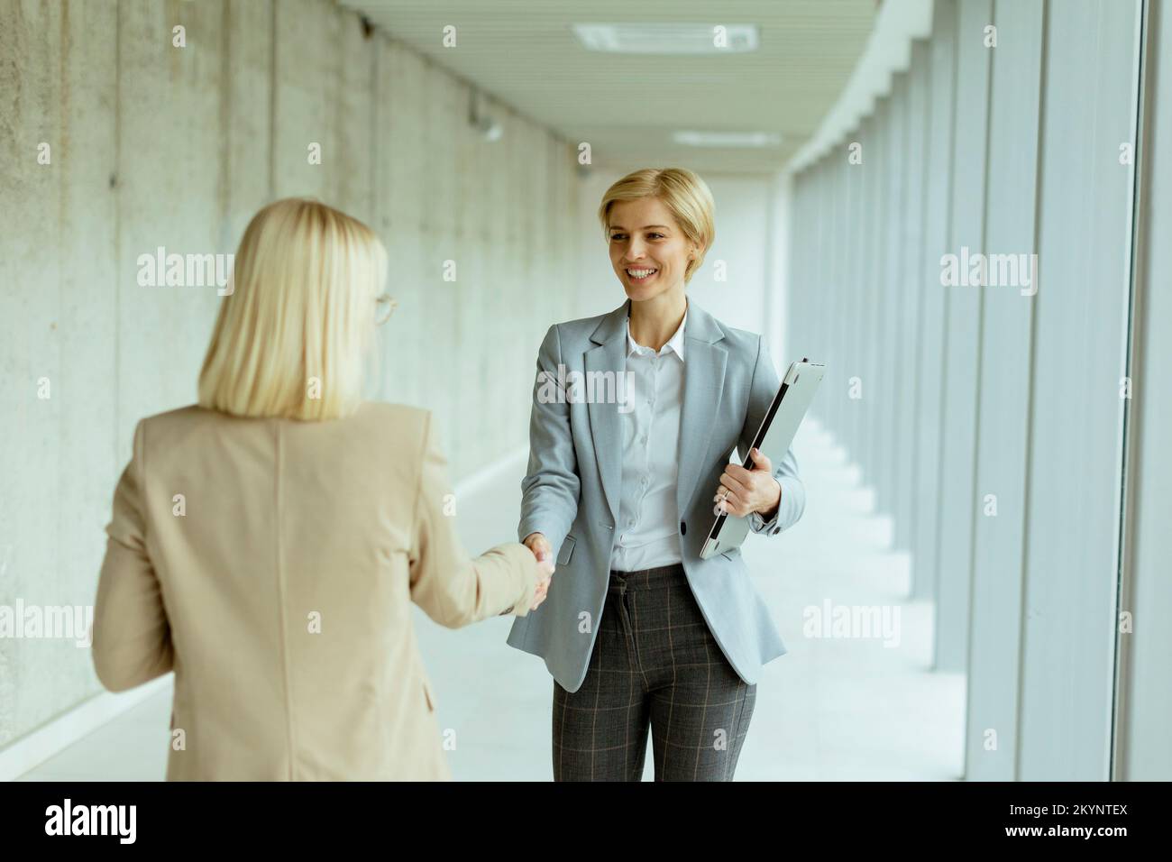 Zwei Geschäftsfrauen, die sich im Büroflur die Hand schütteln Stockfoto