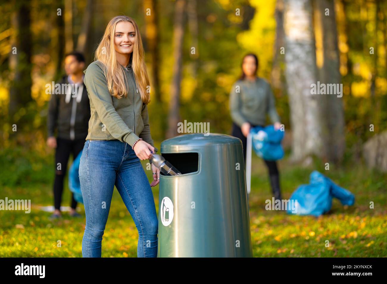 Lächelnde junge Frau, die die Flasche in den Mülleimer wirft Stockfoto