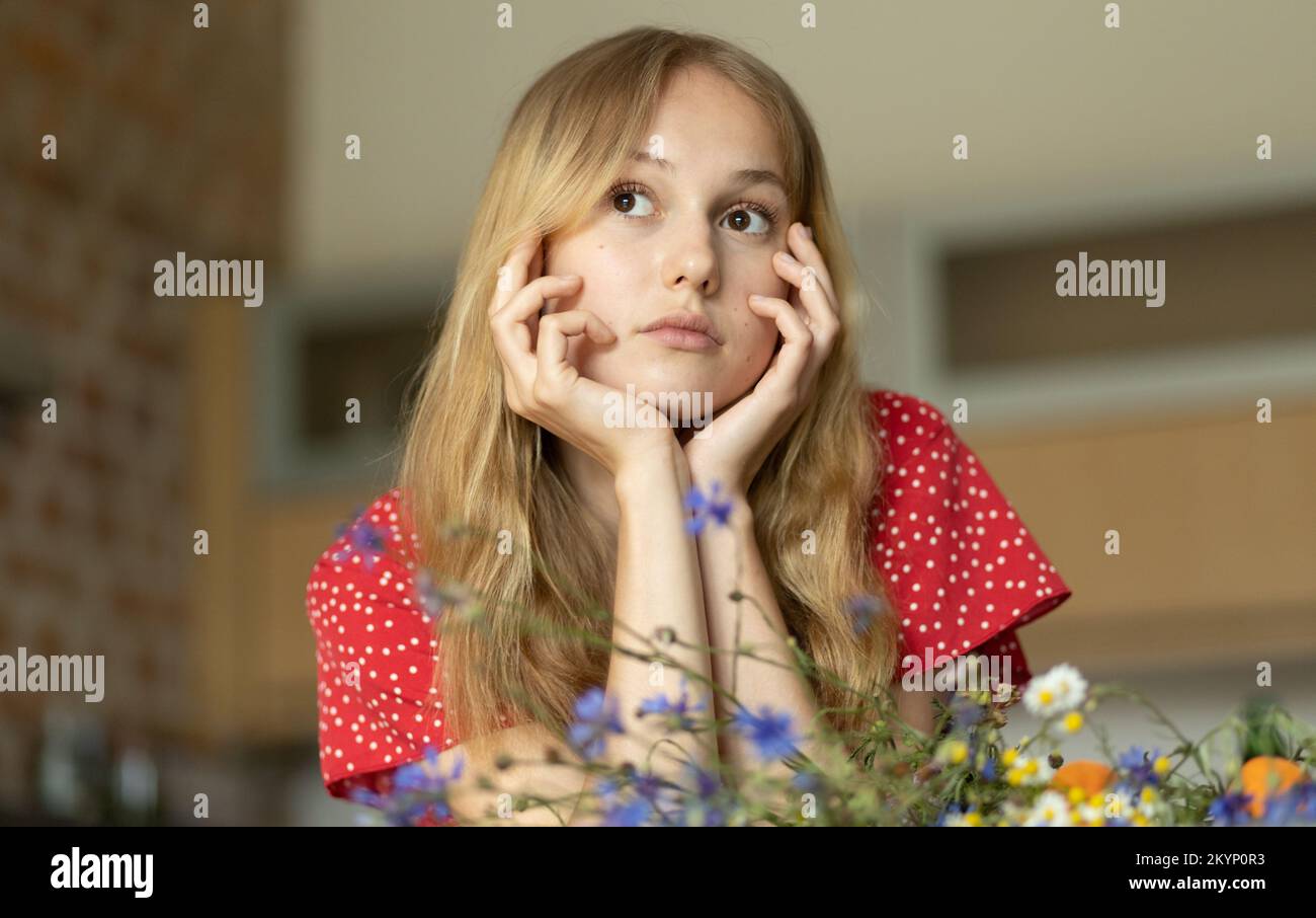 Ein romantisches Mädchen in einem roten Kleid mit einem Strauß wilder Blumen blickt in die Ferne Stockfoto