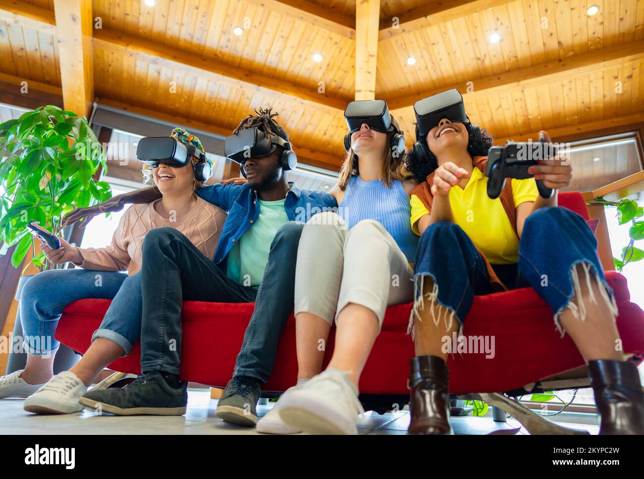 Eine Gruppe internationaler Freunde, die eine neue futuristische virtuelle Technologie mit Headsets tragen, während sie auf dem Sofa sitzen Stockfoto