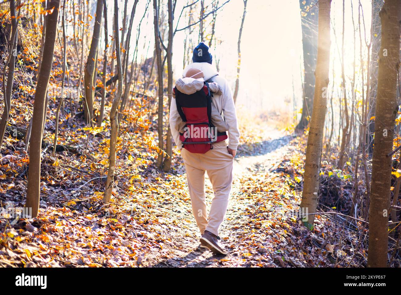 Sportlicher Vater, der seinen kleinen Sohn mit Winteranzug und Mütze im Rucksackträger beim Wandern im Herbstwald trug Stockfoto