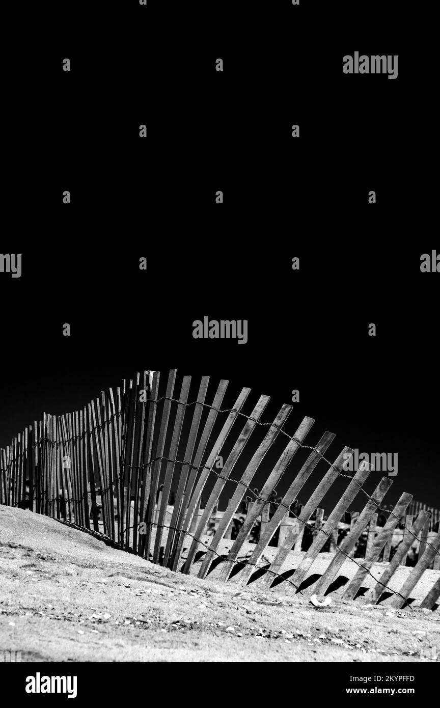 Gedrehter Zaun an einem Sandstrand. Schwarzweißfotografie Stockfoto