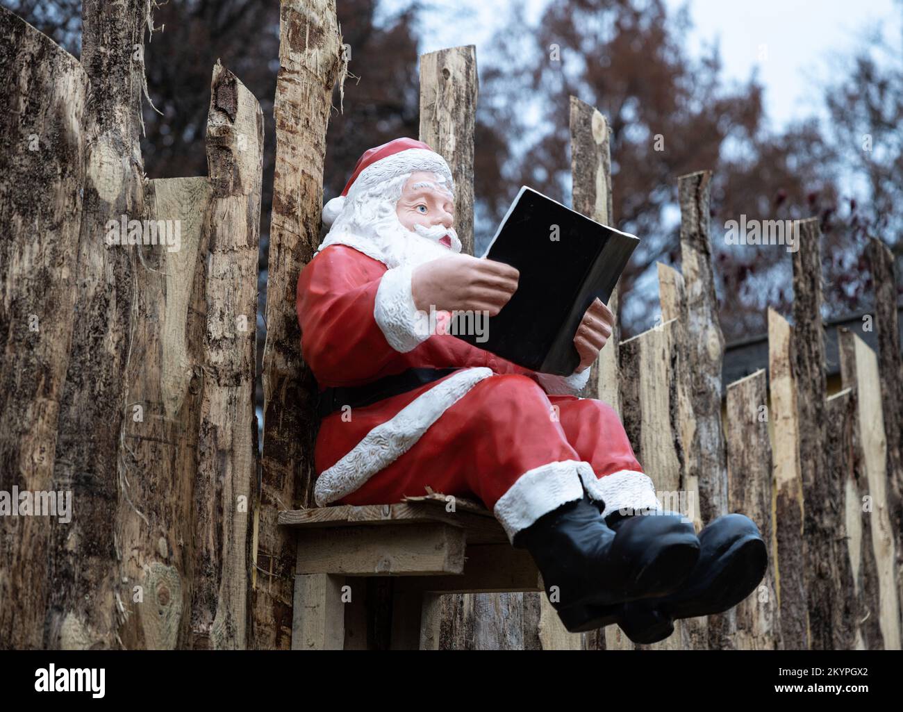 Der Weihnachtsmann sitzt auf einem Holzzaun und hält ein Buch in der Hand Stockfoto