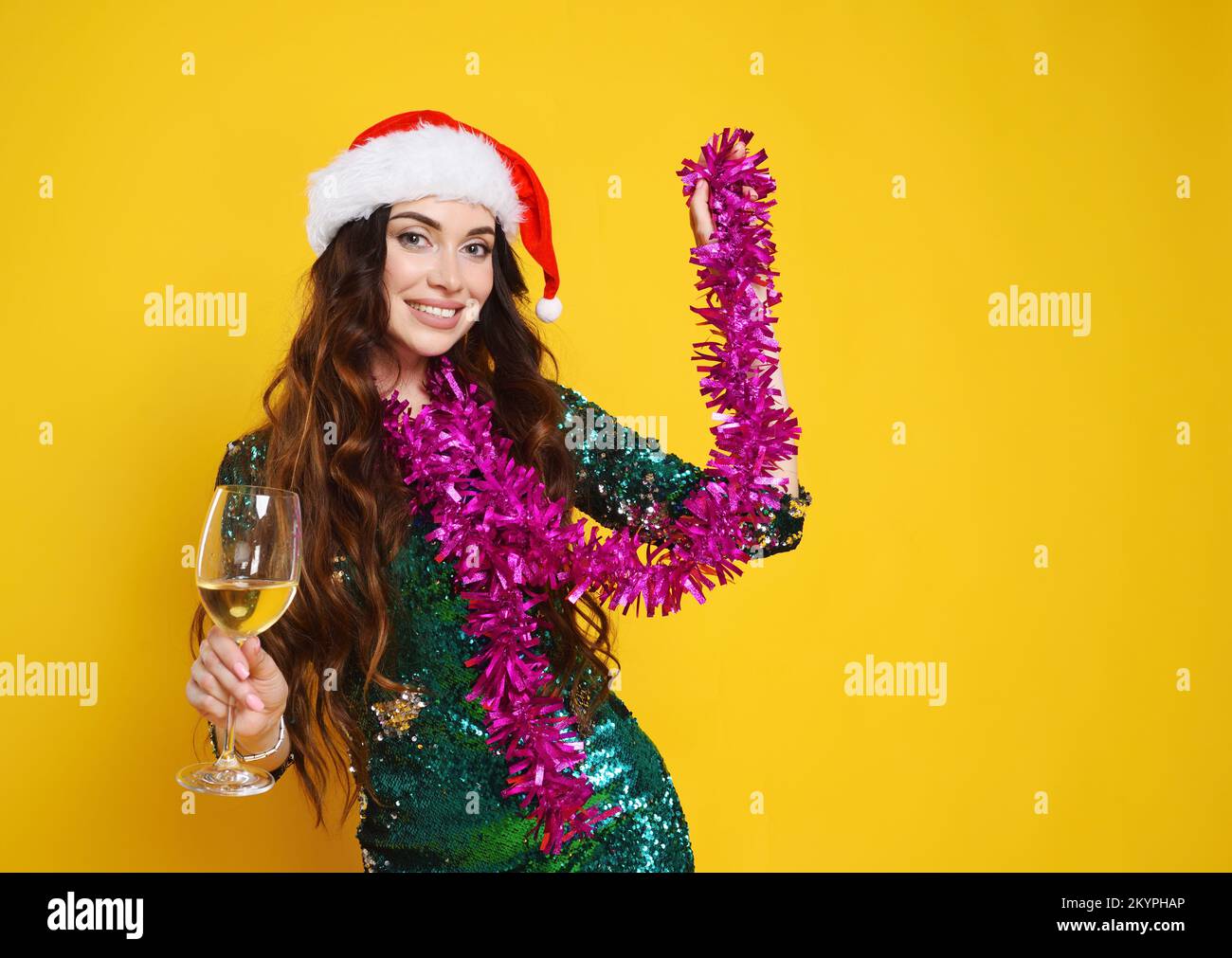Eine Frau in einem grünen, glitzernden Cocktailkleid mit weihnachtsmannmütze in der Hand einer pinkfarbenen Boa und eines Champagnerglases Stockfoto