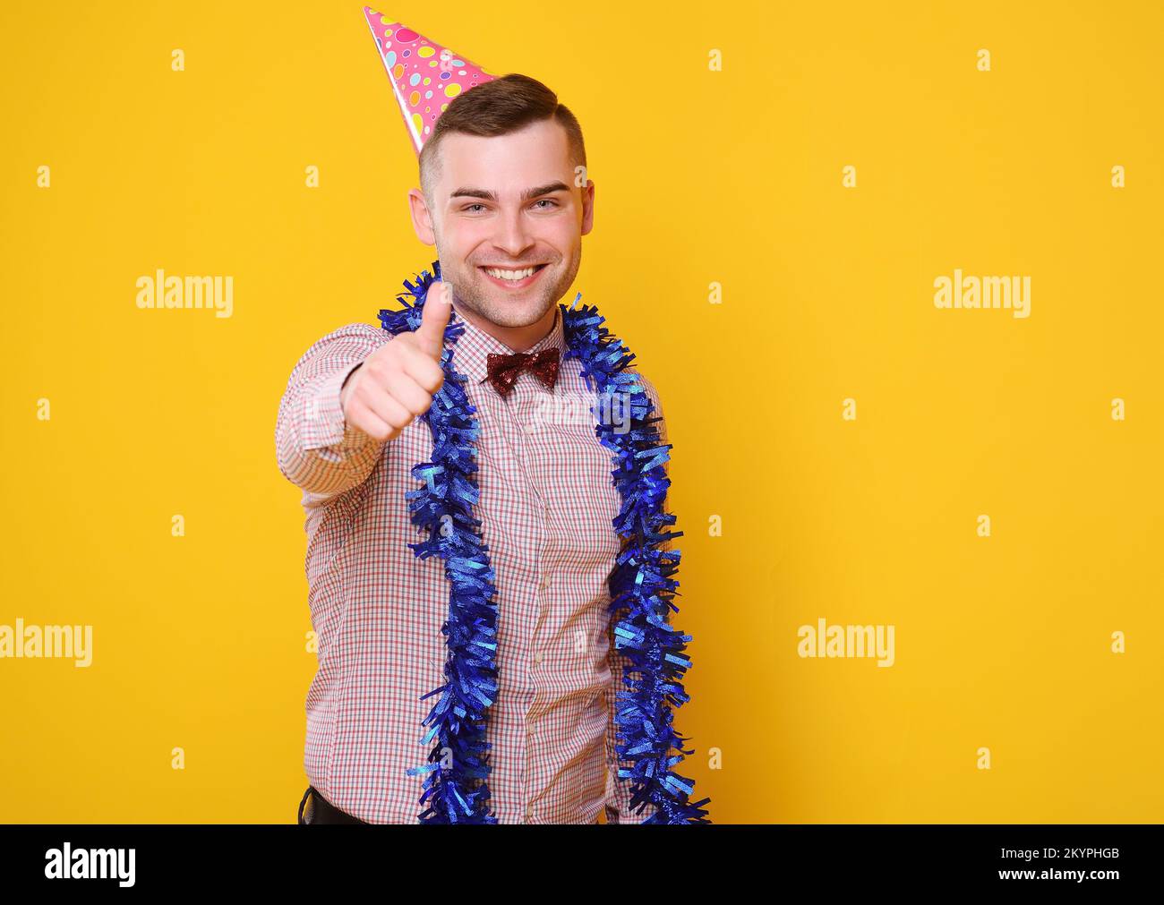 Attraktiver junger Mann mit weihnachtlicher Mütze und blauem boi um den Hals lächelt und zeigt Daumen hoch Stockfoto
