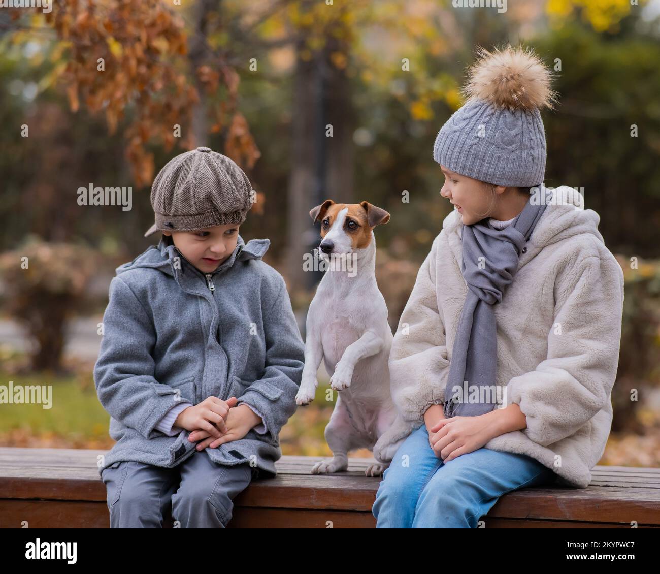 Bruder und Schwester sitzen in einer Umarmung mit einem Hund auf einer Bank für einen Spaziergang im Herbstpark. Junge, Mädchen und Jack russell Terrier. Stockfoto