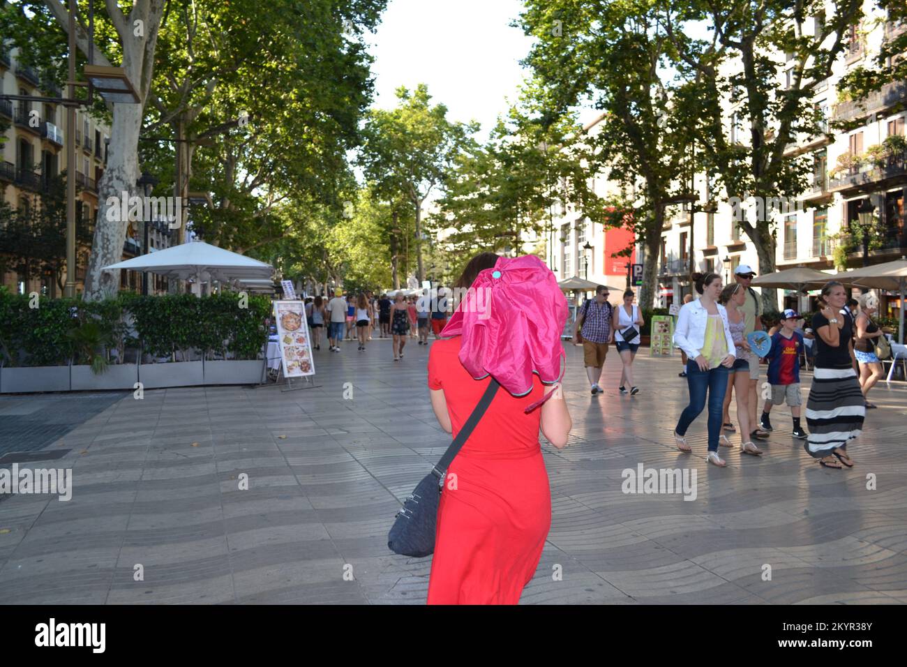 Eine Dame in einem roten Kleid mit einem rosa Regenschirm, die in Barcelona eine Straße entlangläuft. Stockfoto