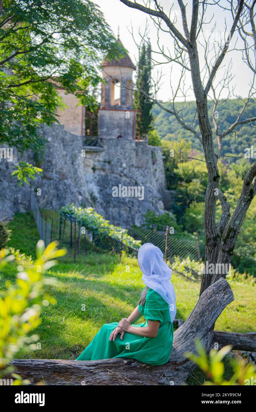 In einem grünen Kleid und Schal sitzt ein Mädchen und sieht sich das Kloster an Stockfoto