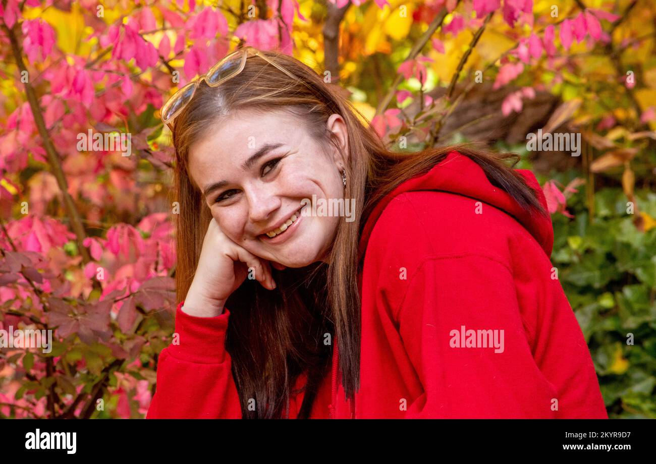 Ein hübscher Teenager in einem roten Sweatshirt posiert an einem hellen Herbsttag Stockfoto