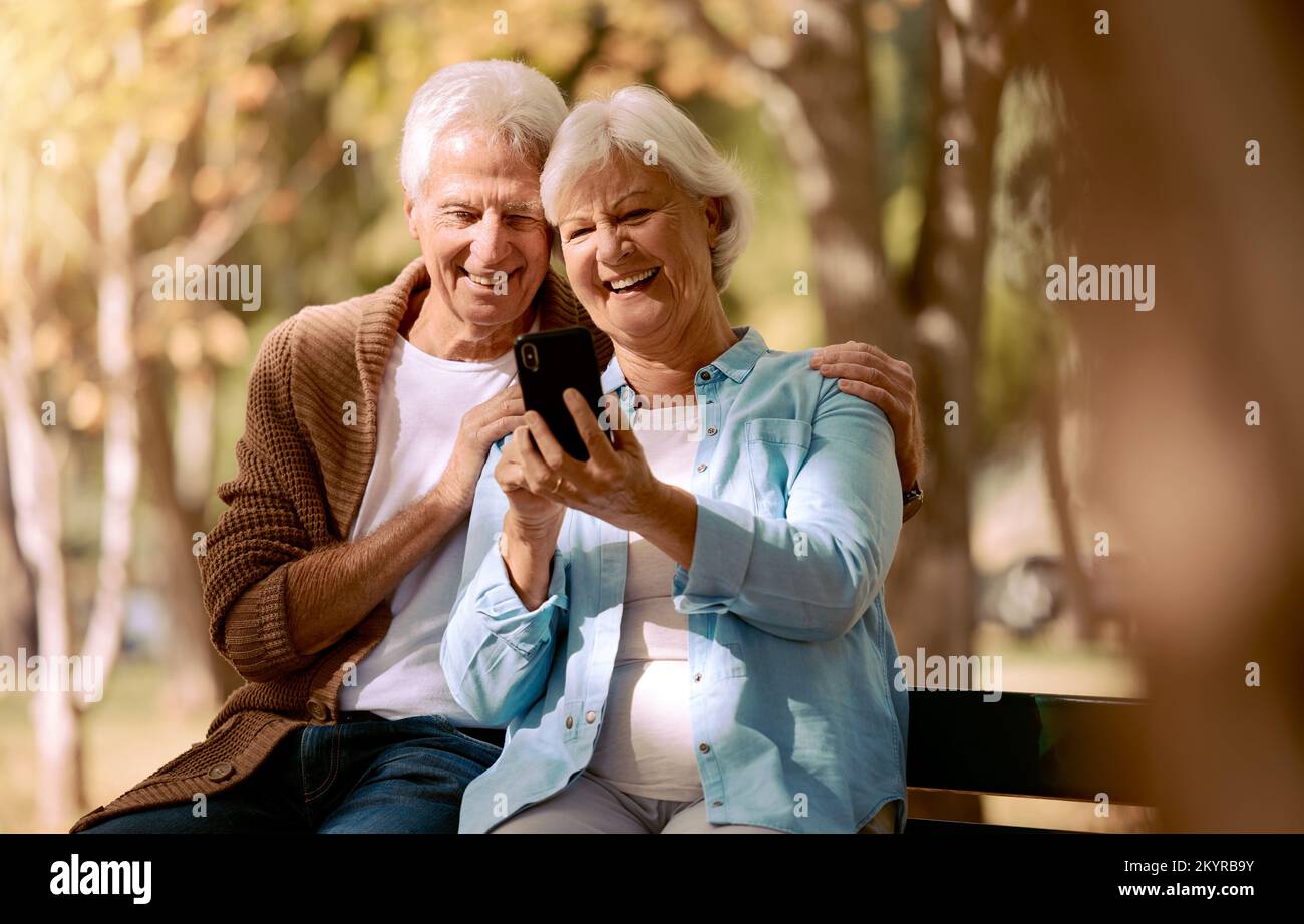 Entspannen Sie sich und telefonieren Sie mit dem alten Paar im Park für Videoanrufe, soziale Medien und Kommunikation. Lächeln, Gesundheit und Internet mit Mann und Frau auf der Bank Stockfoto