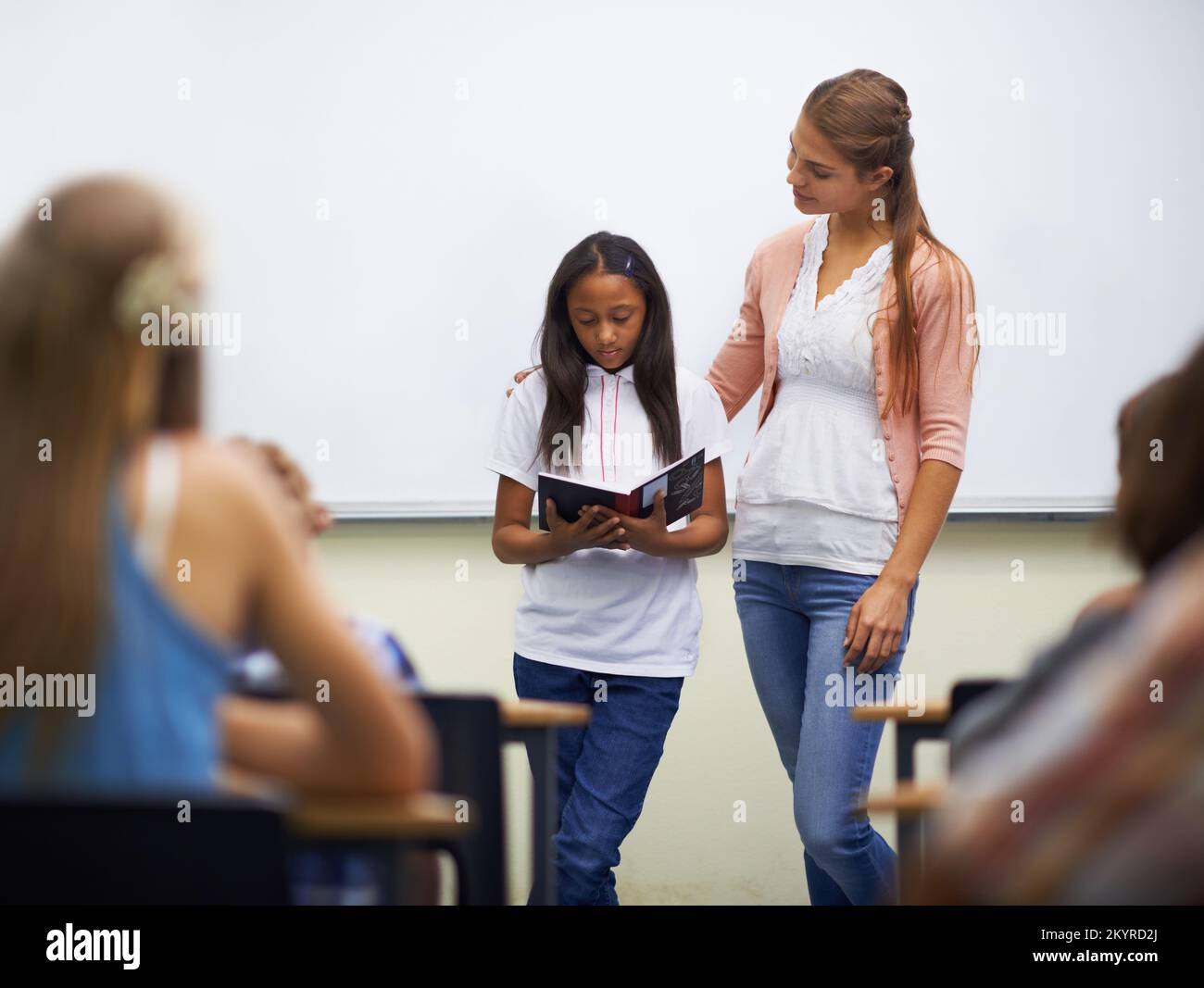 Der beste Buchbericht aller Zeiten. Eine junge Schülerin, die vor dem Klassenzimmer spricht, während ihr Lehrer neben ihr steht. Stockfoto