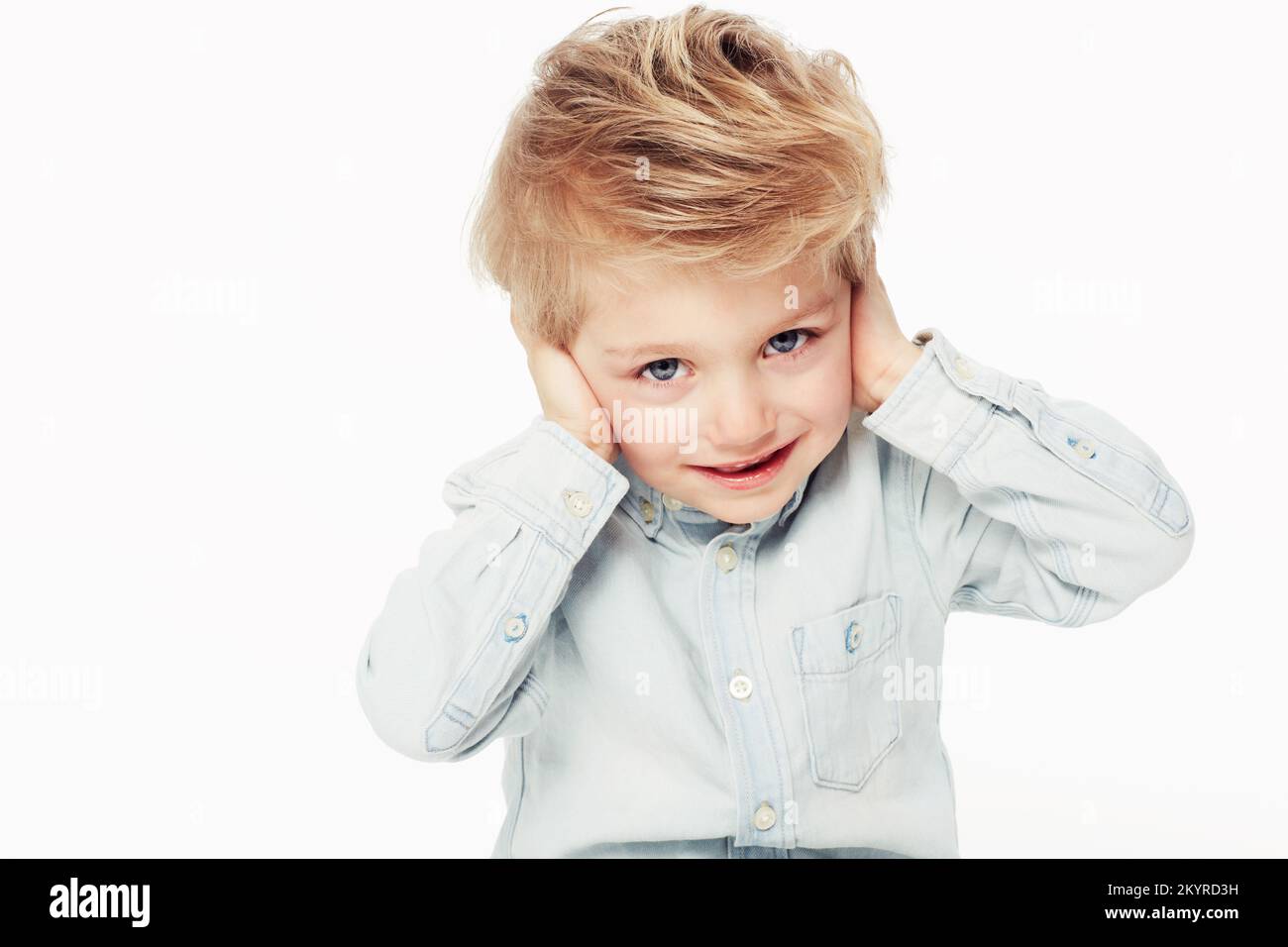 Höre nichts Böses. Ein süßer kleiner Junge, der seine Ohren mit den Händen bedeckt - isoliert. Stockfoto