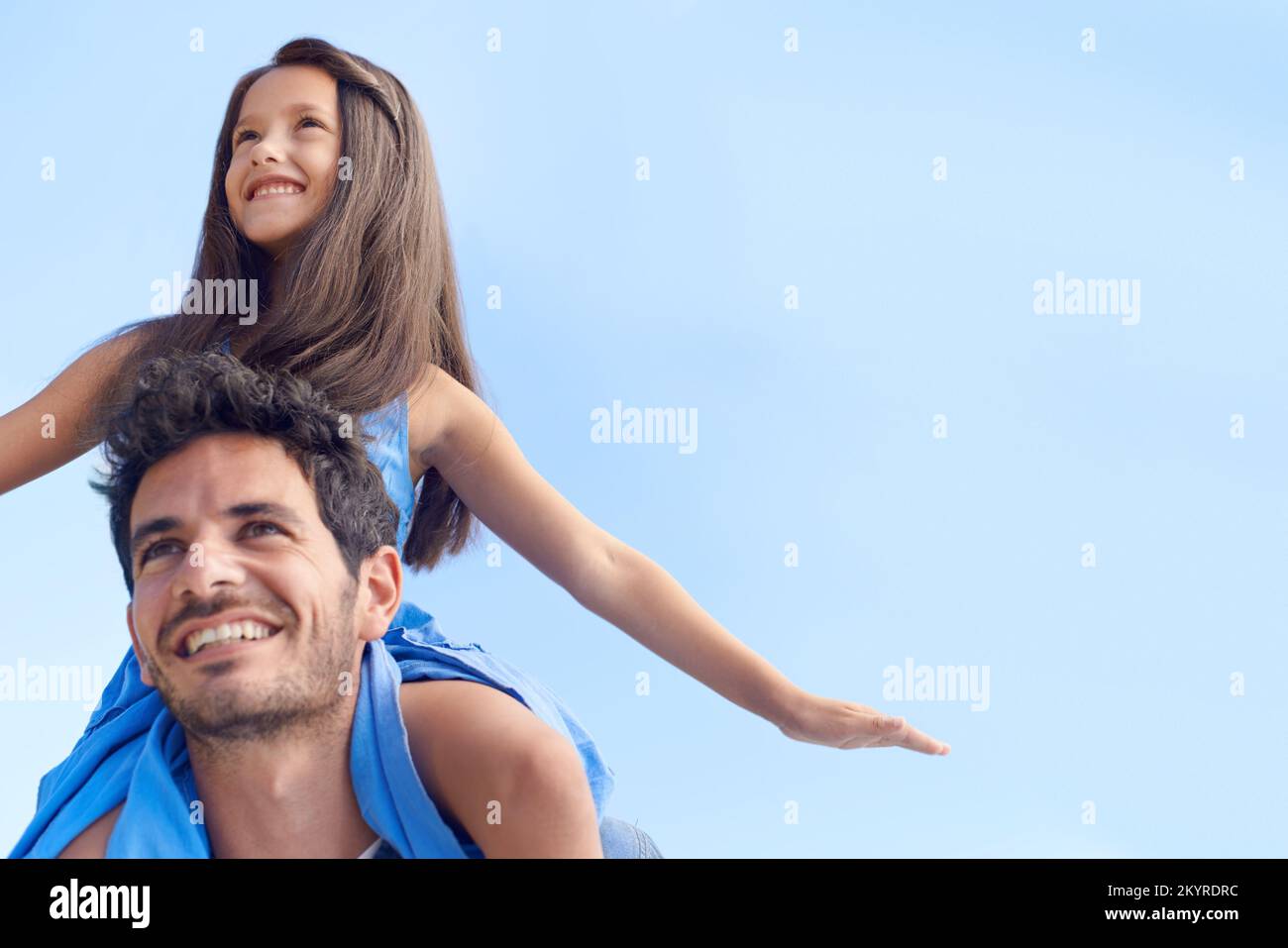 Ich verbringe schöne Zeit mit meiner Tochter. Ein kleines Mädchen, das auf den Schultern des Vaters sitzt, gegen den blauen Himmel. Stockfoto